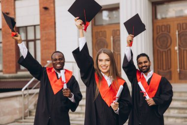 Üç farklı mezun dışarıda başarılarını kutluyor, ellerinde şapkalar ve diplomalar var. Onların ifadeleri mezuniyet gününde neşe ve başarıyı yansıtır..