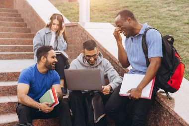 Bir proje için dizüstü bilgisayar ve kitaplar kullanarak kampüs basamaklarında tartışma ve işbirliği yapan çeşitli öğrenci grupları.