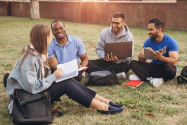 Kampüsün bahçesinde oturan bir grup öğrenci bir çalışma seansına katıldılar. Eğitici konuları tartışmak için dizüstü bilgisayar ve defter kullanıyorlar..