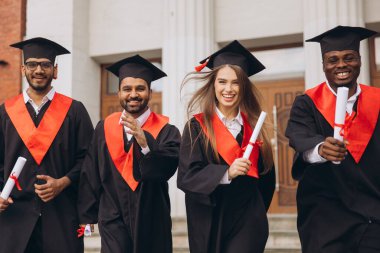 Bir üniversite binasının dışında diplomalarını tutarak, başarıyı ve yeni başlangıçları simgeleyen, kep ve cüppeli çeşitli mezunlardan oluşan neşeli bir grup akademik başarılarını kutluyor..