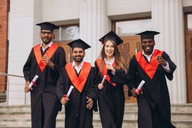 Bir üniversite binasının dışında diplomalarını tutarak, başarıyı ve yeni başlangıçları simgeleyen, kep ve cüppeli çeşitli mezunlardan oluşan neşeli bir grup akademik başarılarını kutluyor..