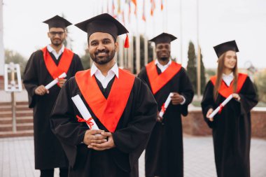 Çeşitli mezunlar başlık ve cübbedeki başarılarını kutlamak için diplomalarını açık havada tutuyorlar. Mezuniyet gününün neşe ve başarısını kucaklamak.