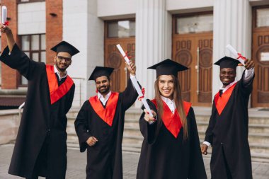 Çeşitli mezunlardan oluşan neşeli bir grup akademik başarılarını gururla kutluyor. Geleneksel elbiseler ve havan tahtaları giyiyorlar. Üniversite binasının önünde diploma tutuyorlar..