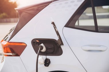 Elektrikli araç güneşin altındaki bir istasyonda şarj oluyor, çevre dostu teknolojiyi ve modern hareketlilik ve çevresel koruma için sürdürülebilir ulaşım seçeneklerini vurguluyor.
