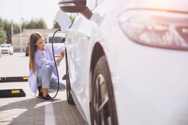 Bir kadın elektrikli aracını güneşli bir kentsel bölgedeki şarj istasyonuna bağlıyor, sürdürülebilir ulaşım ve çevre dostu çözümleri vurguluyor. Bu sahne, modern çevre bilincinin özünü yakalar..