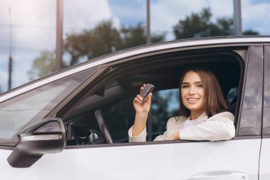 Genç bir kadın modern bir aracın içinde araba anahtarı tutarken gülümsüyor, araba sürmenin verdiği güven ve keyfi gösteriyor. Bağımsızlık, özgürlük ve yeni başlangıçlar temalarını yansıtır.