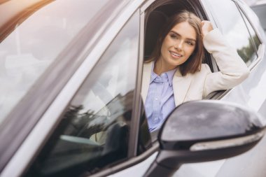 Neşeli bir kadın güneşli bir günün tadını çıkarırken arabanın camından sarkıyor. Beyaz bir ceket ve mavi bir gömlek giyiyor. Mutluluk ve özgürlük yayıyor. Sahne bir rahatlama anı yakalar..