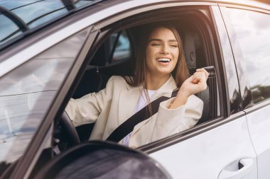 Genç bayan kendinden emin bir şekilde araba kullanıyor, gülümsüyor ve yolculuğun tadını çıkarıyor. Rahat ve mutlu görünüyor, modern bir araçla seyahat ederken özgürlük ve bağımsızlığı yansıtıyor..