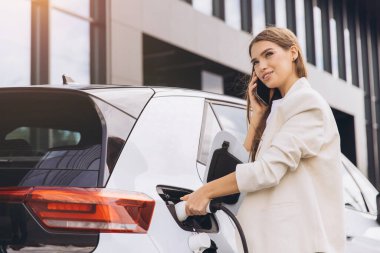 İş dünyasındaki genç bir kadın telefonda konuşurken elektrikli araba kullanıyor. Modern yaşam tarzı ve yenilenebilir enerji kavramı.