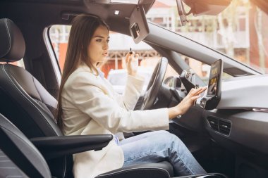 Young woman interacts with a touchscreen in a modern car interior. She is focused and adjusting settings, showcasing the innovation and technology of contemporary vehicles. clipart