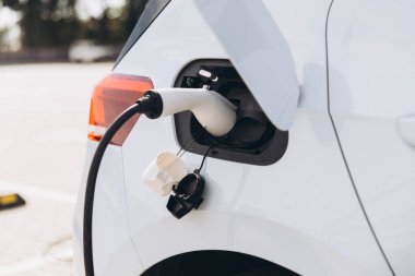 Bir istasyonda şarj edilen elektrikli bir aracın yakın çekim görüntüsü, arabaya bağlı şarj cihazını vurgulamak, sürdürülebilir ulaşım ve temiz enerjiyi vurgulamak.