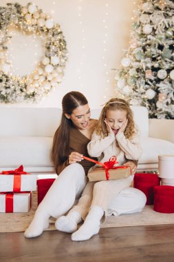 Bir anne ve kızı özel bir bayram anını paylaşıyor, Noel boyunca neşeli dekorasyonlar ve hediye kutularıyla çevrili, neşeli bir ortam yaratıyor ve aile sevgisiyle dolu..