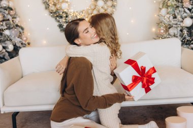 Noel 'de güzel bir şekilde paketlenmiş bir hediyeyi paylaşırken rahat süveter giymiş iki arkadaşın kucaklaşması çok iç açıcı bir sahne. Şenlik ortamı süslenmiş Noel ağaçlarıyla süslenmiş..