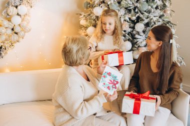 Üç nesildir güzel dekore edilmiş bir ağacın Noel hediyelerini paylaşan neşeli bir aile anı. Sıcak atmosfer, bayram kutlamalarının ve birlikteliğin özünü yansıtıyor..