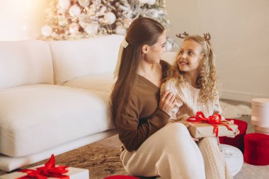 Mutlu bir anne ve kız rahat bir kanepede birlikte oturur, bayram sezonunda hediye paketini paylaşırlar. Oda güzel dekore edilmiş bir Noel ağacı ve çelenkle süslenmiş..