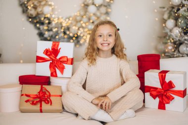 Güzel paketlenmiş Noel hediyeleriyle çevrili rahat bir odada neşeli bir çocuk. Şenlikli dekorasyonlar ve sıcak ışıklar neşeli bir tatil ortamı yaratıyor..