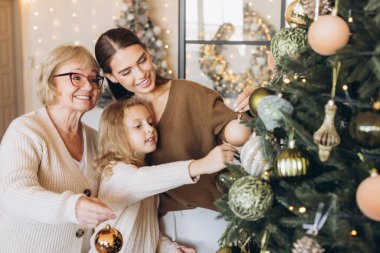 Bir büyükanne, anne ve çocuk olarak neşeli bir aile toplantısı bir Noel ağacını süslerle süsler, tatil sezonunun sıcaklığını ve neşesini sıcacık bir yuva ortamında yakalar..