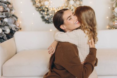 Noel 'de güzel bir şekilde paketlenmiş bir hediyeyi paylaşırken rahat süveter giymiş iki arkadaşın kucaklaşması çok iç açıcı bir sahne. Şenlik ortamı süslenmiş Noel ağaçlarıyla süslenmiş..