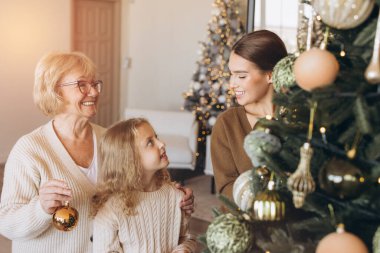 Noel ağacını süs eşyalarıyla süsleyerek, Noel sezonunda birliktelikle süsleyerek birbirine bağlanan üç neslin yer aldığı neşeli bir aile sahnesi. Aile kutlamasının mükemmel tasviri.
