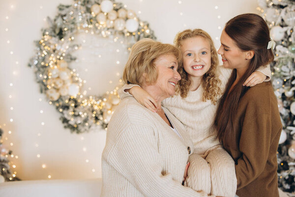A joyful family moment featuring a grandmother, mother, and daughter smiling together. They are celebrating the holiday season with festive decorations, creating a warm and cheerful atmosphere.