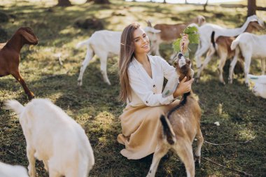 Genç bir kadın güneşli bir çayırda diz çöker, neşeli bir keçiye yapraklar yedirir. Bir sürü tarafından çevrelenmiş sakin çiftlik sahnesi doğayla olan neşe ve bağlantıyı yakalıyor..