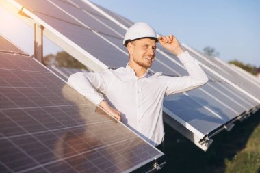 Sert şapka takan kendinden emin erkek mühendis güneşli bir günde güneş panellerini inceliyor. Yenilenebilir enerji ve sürdürülebilir teknoloji kavramı. Yenilikçiliği, verimliliği ve temiz enerji çözümlerini teşvik eder.