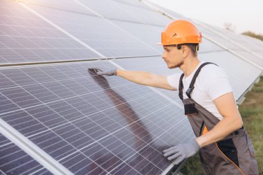 Koruyucu teçhizatta odaklanmış bir teknisyen güneş ışığı altında verimlilik için güneş panellerini inceliyor. Yenilenebilir enerji, sürdürülebilirlik ve modern teknolojiyi temsil eden bu resim, temiz enerji çözümlerinin özünü yakalar..