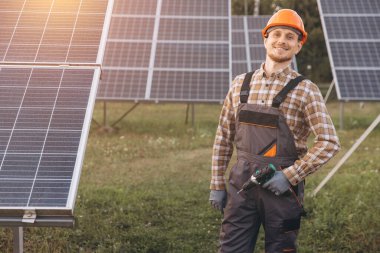 A cheerful solar technician wearing a hard hat stands in a field of solar panels at sunrise, symbolizing renewable energy and sustainable technology. clipart