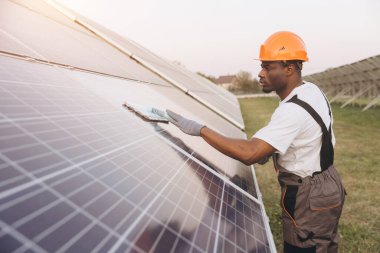 African American dedicated technician cleans large solar panels in an open field under a clear sky, ensuring optimal performance and efficiency of the solar power installation. clipart