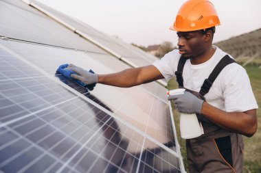 Bir teknisyen, ideal verimliliği sağlamak için profesyonel araçlar kullanarak güneş panellerini ustalıkla temizler. Açık havada yakalanan görüntü yenilenebilir enerji bakımı ve çevresel bilinci vurguluyor.