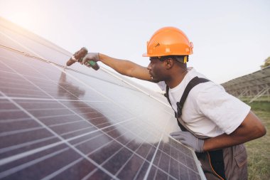 Sert şapka takan profesyonel bir mühendis güneşli bir günde güneş panelleri kuruyor. Sürdürülebilir enerji çözümlerine odaklanmış, yenilenebilir enerji üretimini artırmak için hassasiyetle çalışıyor.