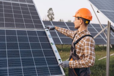 Güvenlik teçhizatı takan profesyonel bir mühendis bir alanda güneş panellerini inceliyor. Bu görüntü yenilenebilir enerji, yeşil teknoloji ve sürdürülebilir güç çözümlerine odaklanır..
