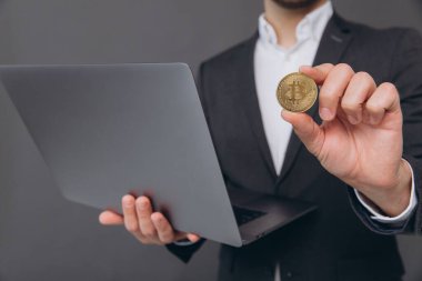 Gri arkaplan üzerinde dizüstü bilgisayar tutarken Bitcoin gösteren neşeli bir işadamının yakın plan portresi