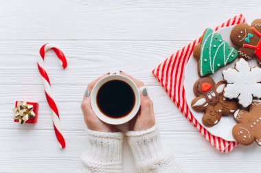 Sıcak kış sahnesinde kahve tutan eller, bir tabak şenlikli kurabiye, baston şekerler ve bir hediye kutusu. Tatil toplantıları ve Noel kutlamaları için mükemmel..