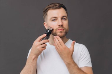 Sakal tıraşı makinesi, portre ya da banyo rutini olan mutlu bir adam, cilt bakımı. Yüz temizleme, yüz bakımı ya da stüdyo çalışanı mutluluğu gri arka planda