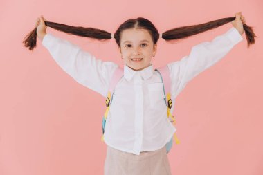 Sırt çantalı, uzun saçlı ve pembe arka planda suratını buruşturan okul üniformalı şirin bir kız.