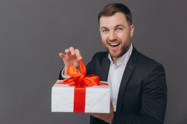 Sakallı mutlu gülen adam elinde bir hediye tutuyor ve onu gri bir arkaplanda açıyor. Sevgililer günü, Noel ve yeni yıl konsepti.