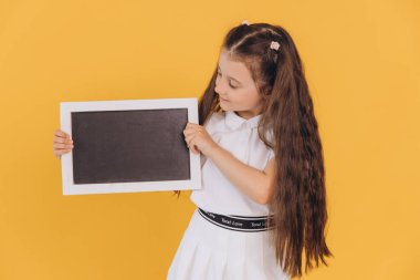 Küçük liseli kız mesajın için karatahta tutuyor. Kopya alanı. Okul reklamı için sarı arka planda kara tahtası olan birinci sınıf öğrencisi.