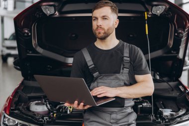 Tamirci tamirci, araba tamirhanesinde dizüstü bilgisayarla araba kontrol ediyor. Mühendis genç adam aracın detaylarına bakıyor..