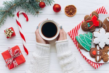 Sıcak bir fincan kahve, şenlikli kurabiyeler ve Noel süslemelerinin olduğu rahat bir masa üstü sahnesi. Görüntü, bayram neşesini hediyelerle, baston şekerlerle ve canlı, mevsimsel renklerle yayar..