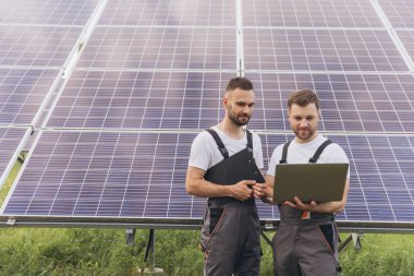 Güneş paneli inşaatının verimliliğini kontrol etmek için dijital tablet okuma bilgisi kullanan bir enerji uzmanı. Yeşil enerji işleri. Teknoloji. İki güneş enerjisi santrali işçisi veri kaydediyor