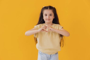 Aşk Konsepti. Sevimli küçük kız Stüdyoda elleri sarı arkaplan üzerinde kalp hareketi yapıyor.