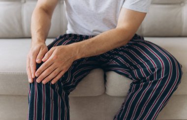 Koltukta oturan adam diz ağrısından muzdarip. Acılı dizine masaj yapan olgun bir adam. Evde diz ağrısı çeken bir adam var, kapatın..