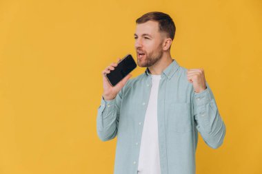 30 'lu yaşlardaki mutlu Hintli genç adam el ele tutuşmuş cep telefonuyla sohbet ediyor sarı arka planda izole edilmiş bir jest yapıyor.