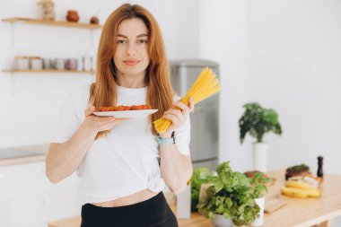 Evde, mutfakta spagetti ve ev yapımı domates sosu pişiren kaslı, güzel bir kadın.