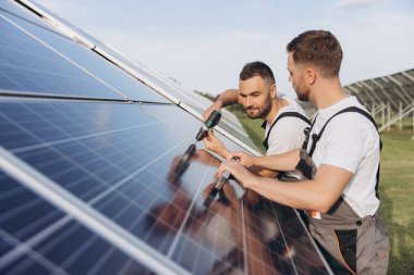 Gri üniforma giyen iki yetenekli işçi veya zanaatkar, teknisyenler temiz enerji ve elektrik tedariği için güneş panelleri kuruyorlar.