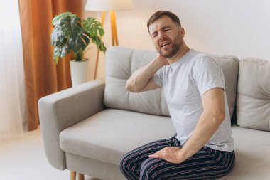 Boyun ağrısı. Kafkasyalı bir adam evdeki oturma odasında boynuna masaj yapıyor. Kemik eklem iltihabı, Sağlık Sorunu Kavramı.