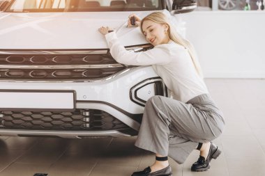 Bayilikte yeni arabasına sarılan olumlu, genç, beyaz bir kadın. Mutlu kadın sonunda uzun zamandır beklenen arabaya kavuştu.