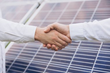 Güneş enerjisi istasyonundaki güneş panellerinin kurulumu ve bakımını denetlemek için çalıştıktan sonra iki Elektrik Mühendisi el sıkışıyor.
