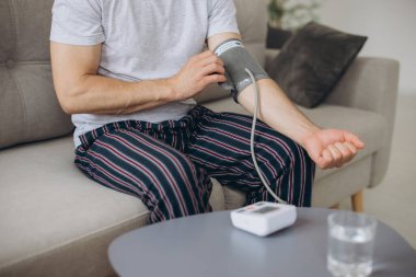 Evdeki kanepede oturan erkek, kan basıncını ölçüyor. Modern tonometre kullanan bir adam stresten kaynaklanan hipertansiyonu hisseder.